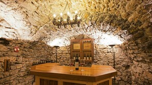Un espace bar aux murs de pierre, avec un comptoir en bois, des bouteilles de vin, des verres et un lustre.