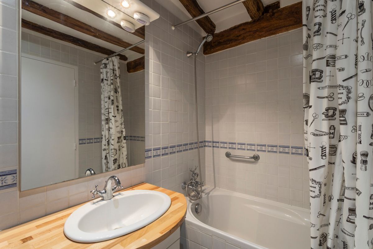 Une salle de bain avec un meuble-lavabo en bois, un lavabo blanc, une baignoire et un rideau de douche à motifs.
