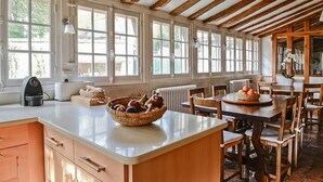 A kitchen with wooden beams, large windows, and a central island with a fruit bowl.