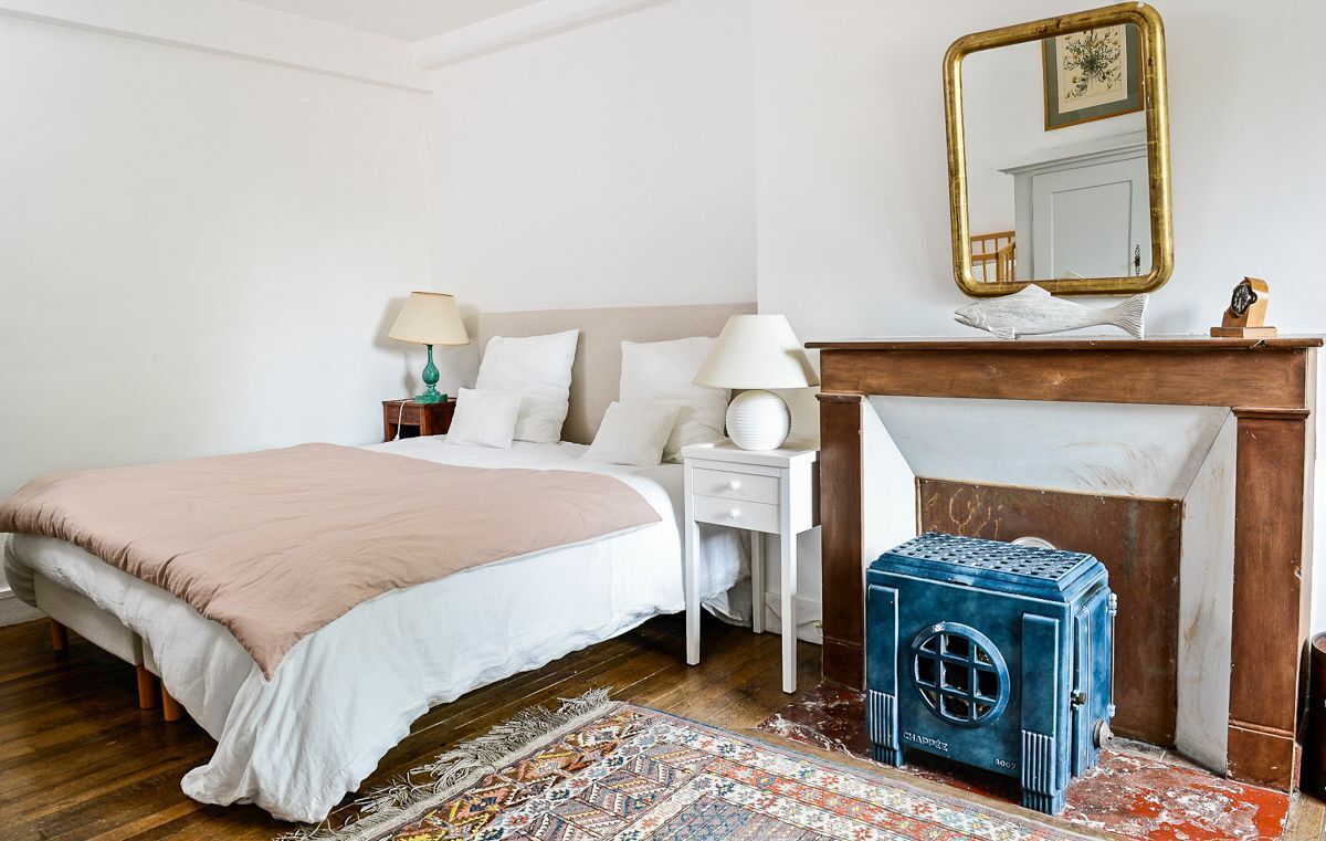 Un dormitorio con una cama grande, mesitas de noche con lámparas, una chimenea y un espejo decorativo.