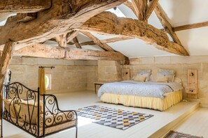 Une chambre avec un lit, une chaise, un plafond avec une poutre en bois et un mur en pierre.