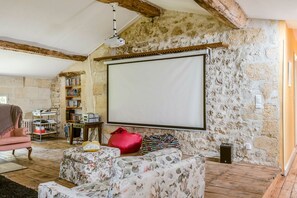 Une pièce chaleureuse avec un mur en pierre, un écran de projection, une bibliothèque et un fauteuil rose.