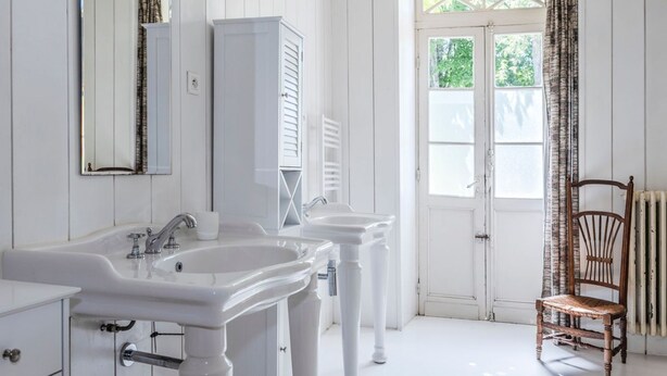 Une salle de bain avec deux lavabos blancs, un miroir et une chaise en bois.