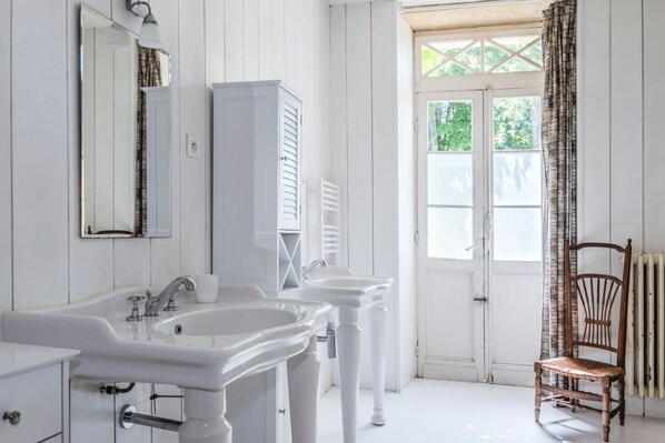 A bathroom with two white sinks, a mirror, and a wooden chair.