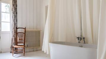 Een badkamer met een badkuip, een houten stoel, een radiator en een raam met gordijnen.