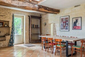 A rustic dining area with a wooden table and chairs, a bookshelf, and a door leading to an outdoor area.