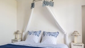Une chambre à coucher avec un lit à baldaquin, du linge de lit blanc et des coussins à motifs floraux. Il y a deux tables de chevet avec des lampes.