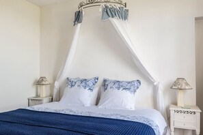 A bedroom with a canopy bed, white bedding, and floral-patterned pillows. There are two bedside tables with lamps.