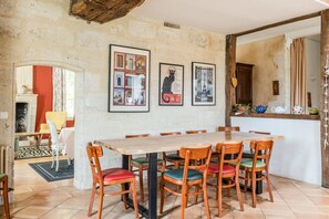 Un coin repas avec une table et des chaises en bois, des tableaux encadrés au mur et une vue sur une autre pièce.