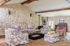 Una habitación rústica con paredes de piedra, techo de madera y una mezcla de mobiliario tapizado con motivos florales y color rosa.