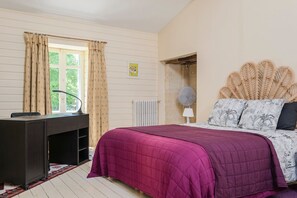A bedroom with a bed, a desk, a radiator, and a window with curtains.