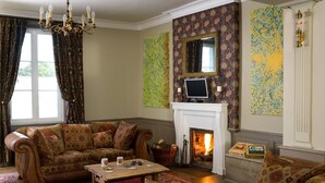 A traditional living room with a fireplace, patterned wallpaper, and classic furniture.
