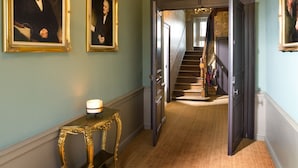 A hallway with two framed portraits, a staircase, and a table with a candle.