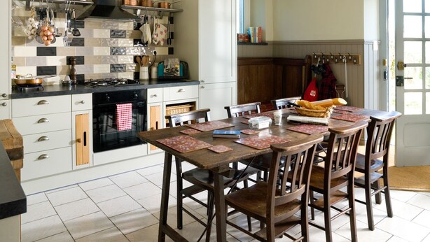 A kitchen with a stove, oven, and hanging utensils; a dining table with chairs; and a door with a coat rack.