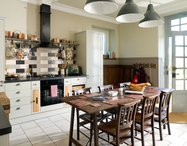 Una cocina con estufa, horno y utensilios colgando; una mesa de comedor con sillas; y una puerta con perchero.