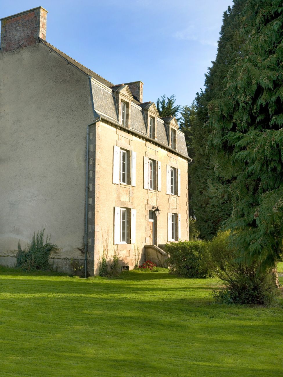 Un grand bâtiment en pierre à deux étages, doté d’une façade symétrique, d’une entrée centrale avec un petit porche et d’une pelouse bien entretenue à l’avant.