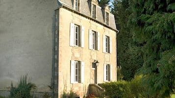 Un grand bâtiment en pierre à deux étages, doté d’une façade symétrique, d’une entrée centrale avec un petit porche et d’une pelouse bien entretenue à l’avant.