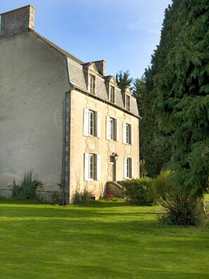 Un grand bâtiment en pierre à deux étages, doté d’une façade symétrique, d’une entrée centrale avec un petit porche et d’une pelouse bien entretenue à l’avant.