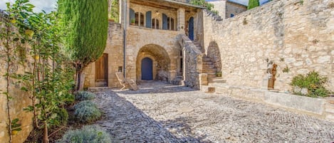 A stone building with a courtyard, arched doorways, and a staircase leading to an upper level.
