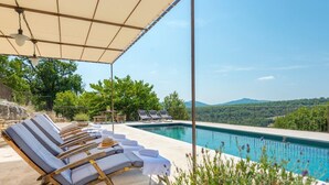 Un área junto a la piscina con sillas de descanso y una zona de estar cubierta.