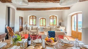Comedor con una mesa dispuesta para una comida, con pan, fruta y vino. Hay tres ventanas arqueadas que ofrecen luz natural y vistas al exterior.