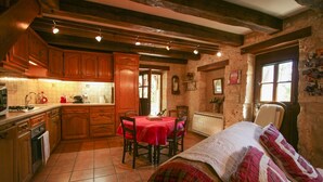 Eine rustikale Küche mit Holzausbau, einem Esstisch mit Stühlen und einem Bett mit karierter Decke.