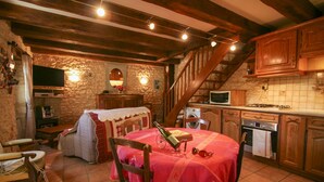 Eine rustikale Küche mit Holzausbau, einer Steinwand, einem Esstisch mit roter Tischdecke und einer Treppe, die zu einer oberen Ebene führt.