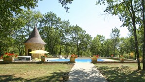 Ein Steinhaus mit einem Kegeldach, einem Schwimmbad und Sitzgelegenheiten im Freien mit Sonnenschirmen.