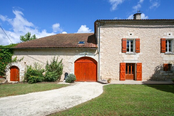 Un bâtiment en pierre avec un toit en tuiles, deux portes en bois et une allée gravillonnée.