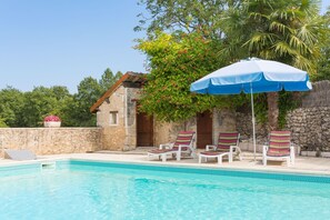 A poolside area with a stone building, a blue umbrella, and colorful lounge chairs.