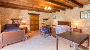 Una habitación rústica con techo de madera, una cama, un escritorio, una silla y una pared de piedra.