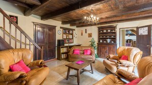 Un interior tradicional con vigas de madera, mobiliario de cuero, una araña y una escalera.
