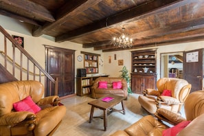 A traditional interior with wooden beams, leather furniture, a chandelier, and a staircase.