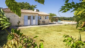 Una casa de piedra rústica con techo de tejas, un pequeño jardín y una zona de piscina.