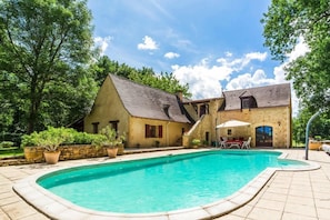 Een huis met een zwembad, een terras met tuinmeubels, en een stenen muur.