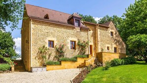 Un bâtiment en pierre avec un toit rouge, une allée en gravier et une pelouse bien entretenue.