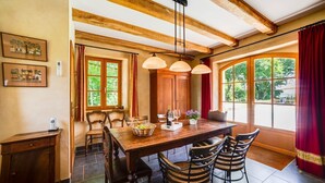 Un coin repas avec une table en bois, quatre chaises, un lustre et de grandes fenêtres avec des rideaux.