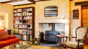 Un salon chaleureux avec une cheminée, des étagères à livres, un canapé rouge et un fauteuil à motifs floraux.