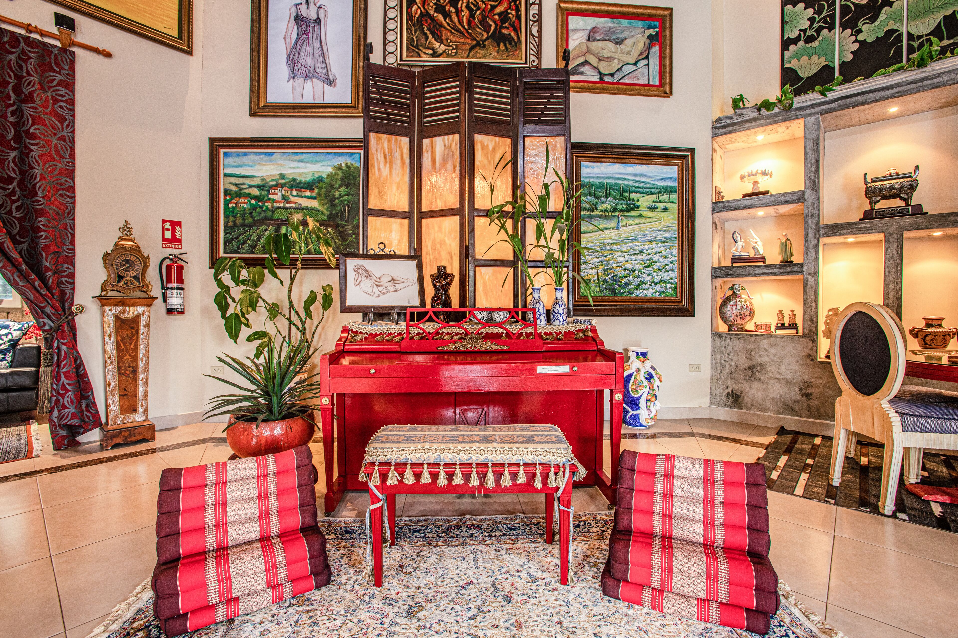 A room with a red piano, a bench, a potted plant, and framed artwork on the walls.