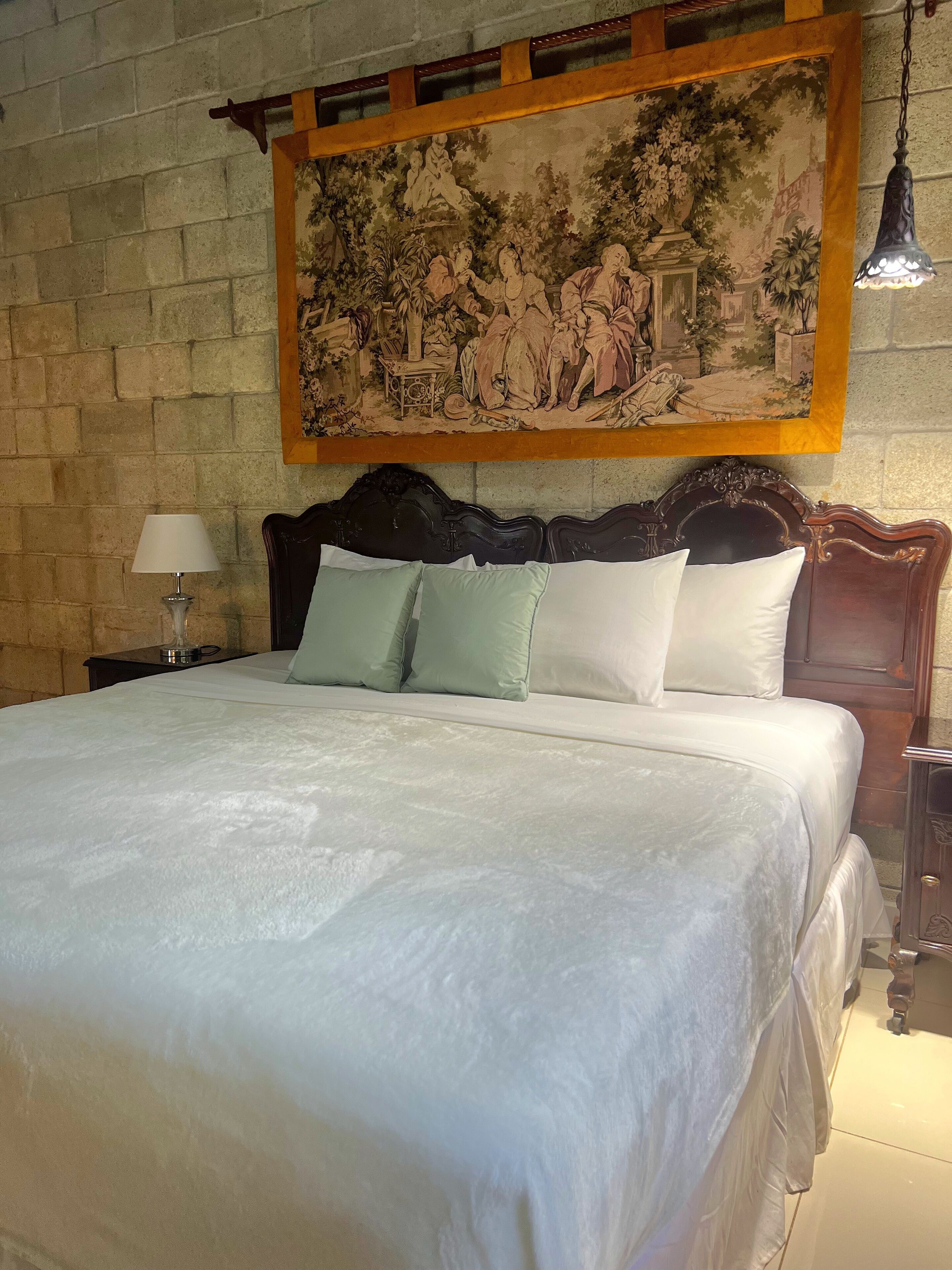 A bed with a wooden headboard, a nightstand with a lamp, and a painting above the bed.