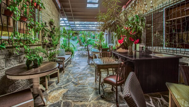 Un jardín interior acogedor con suelo de piedra, mobiliario de madera y diversas plantas en macetas.