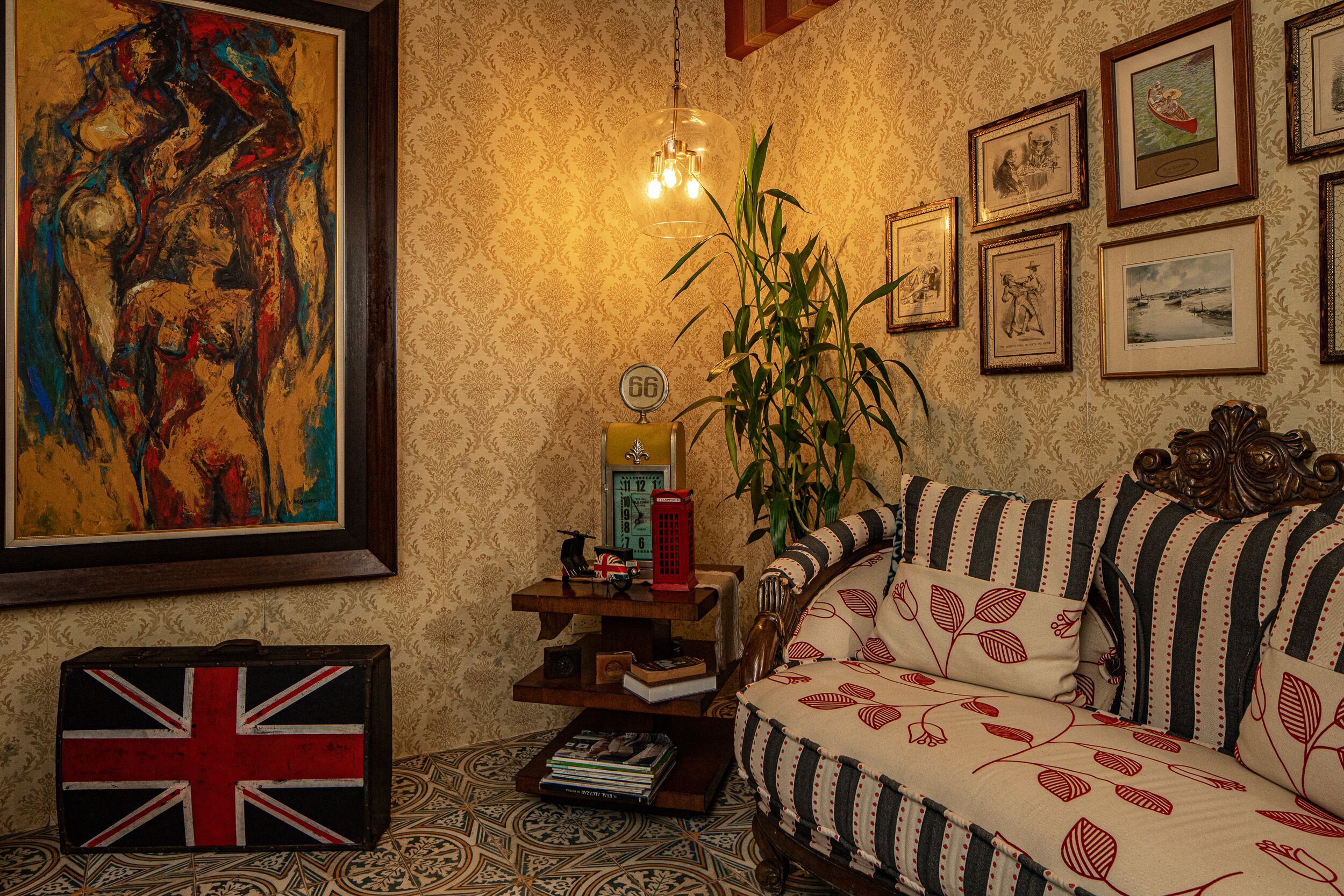 Een kamer met behang met een patroon, een groot abstract schilderij, een bank met gestreepte kussens, een plant en een vintage telefoon.