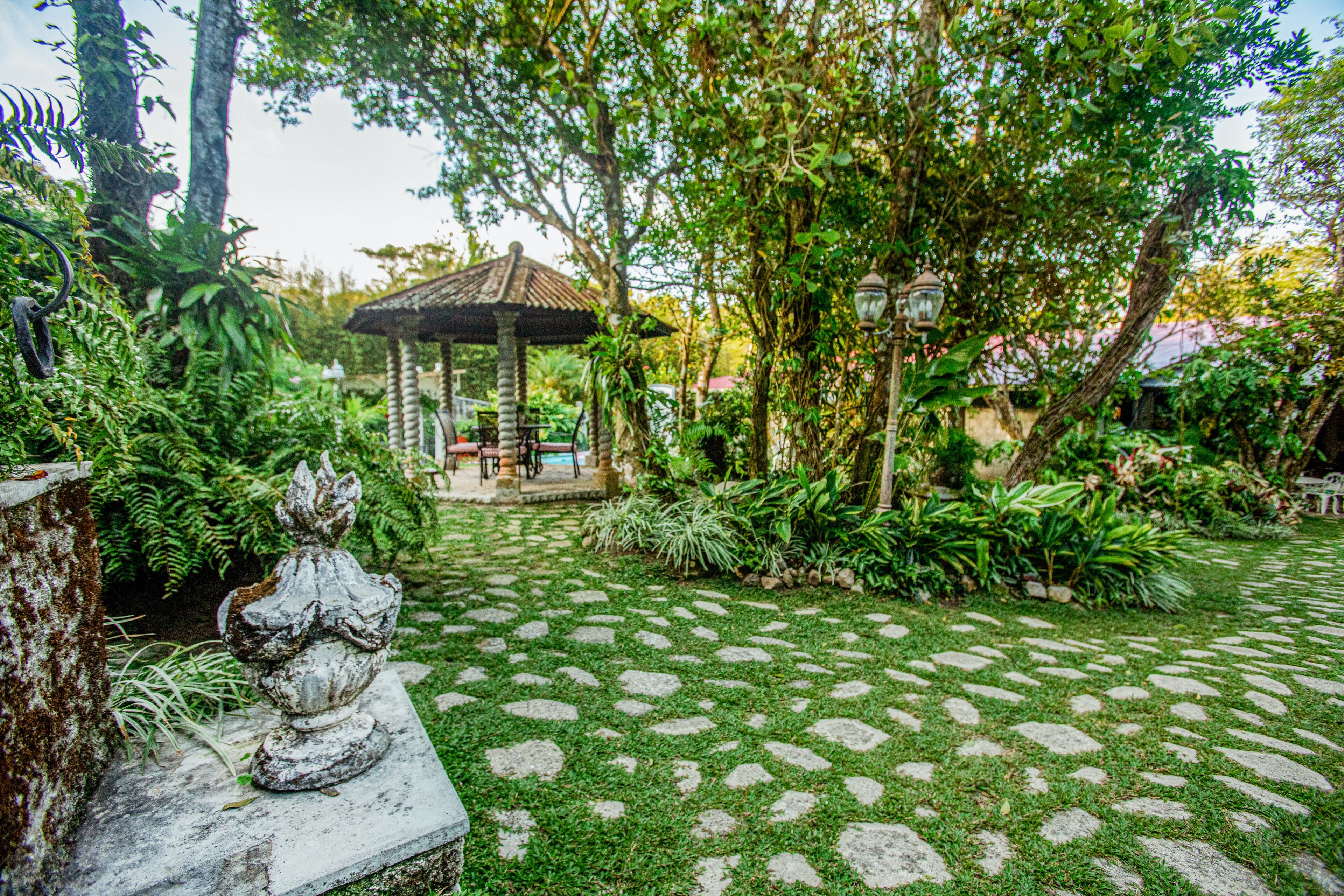 Un jardín con un pabellón, un sendero de piedra y abundante vegetación.