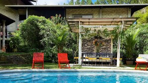 Una piscina con sillas rojas y una pérgola con un muro decorado.