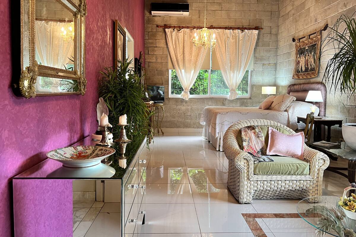 A room with a bed, a wicker chair, a glass table, a mirror, and a television.