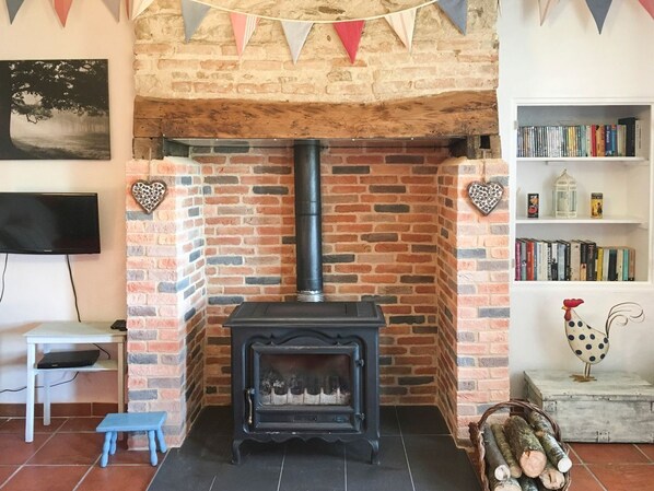 A cozy living room with a brick fireplace, a television, a bookshelf, and a small table.