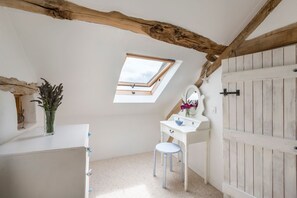 A small, white, attic-style bedroom with a skylight, a white vanity with a mirror, and a wooden wardrobe.
