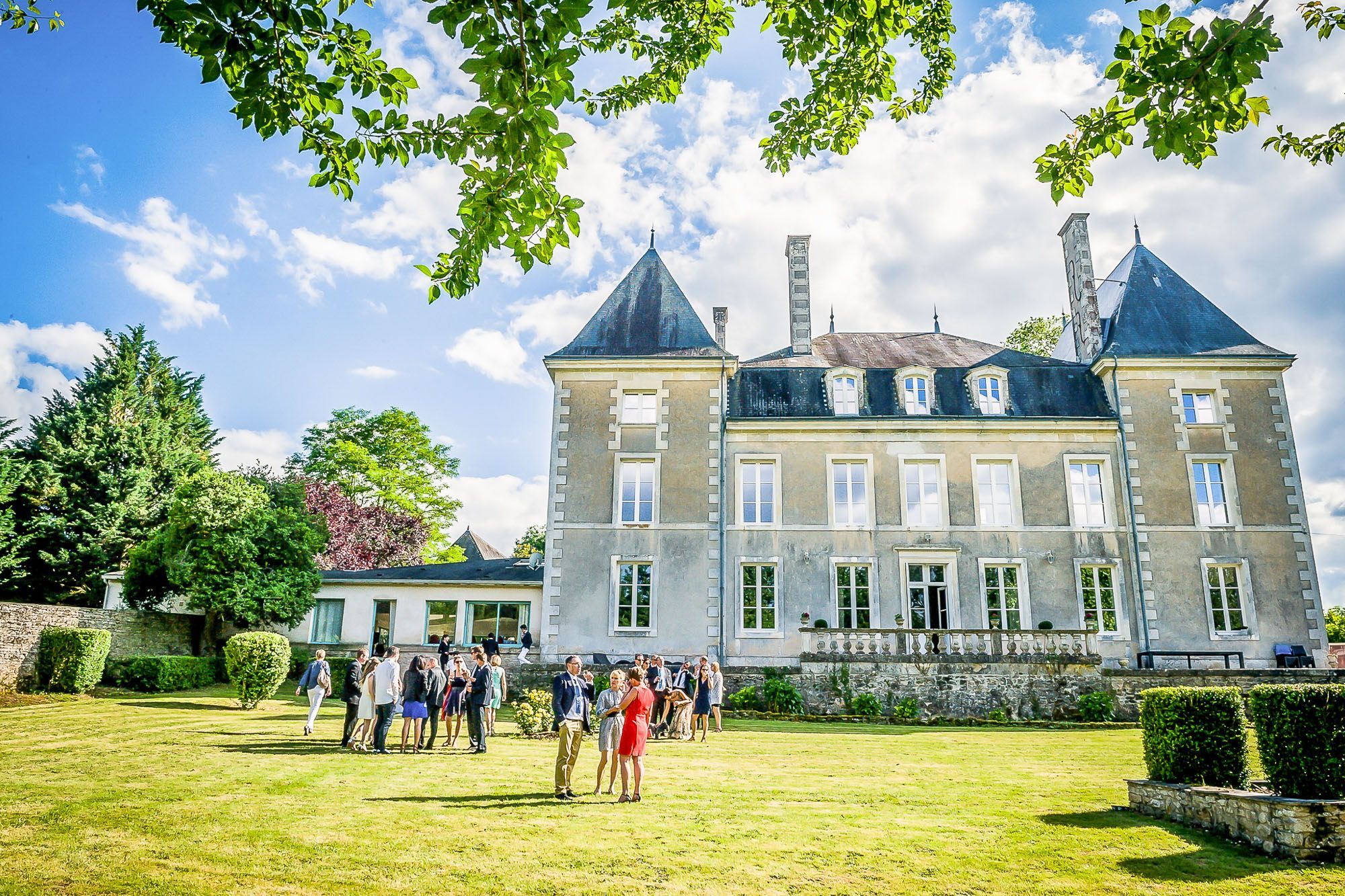 Un grand bâtiment historique doté de nombreuses fenêtres et d’une tour centrale, entouré d’une pelouse bien entretenue et d’arbres.