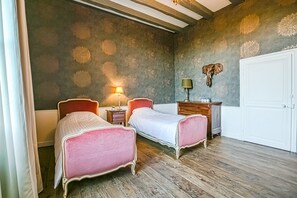 A bedroom with two beds, a nightstand with a lamp, a dresser, and a door. - Chateau Paradis - Twentyeight Bedroom Castle, Sleeps 91 (Benest)