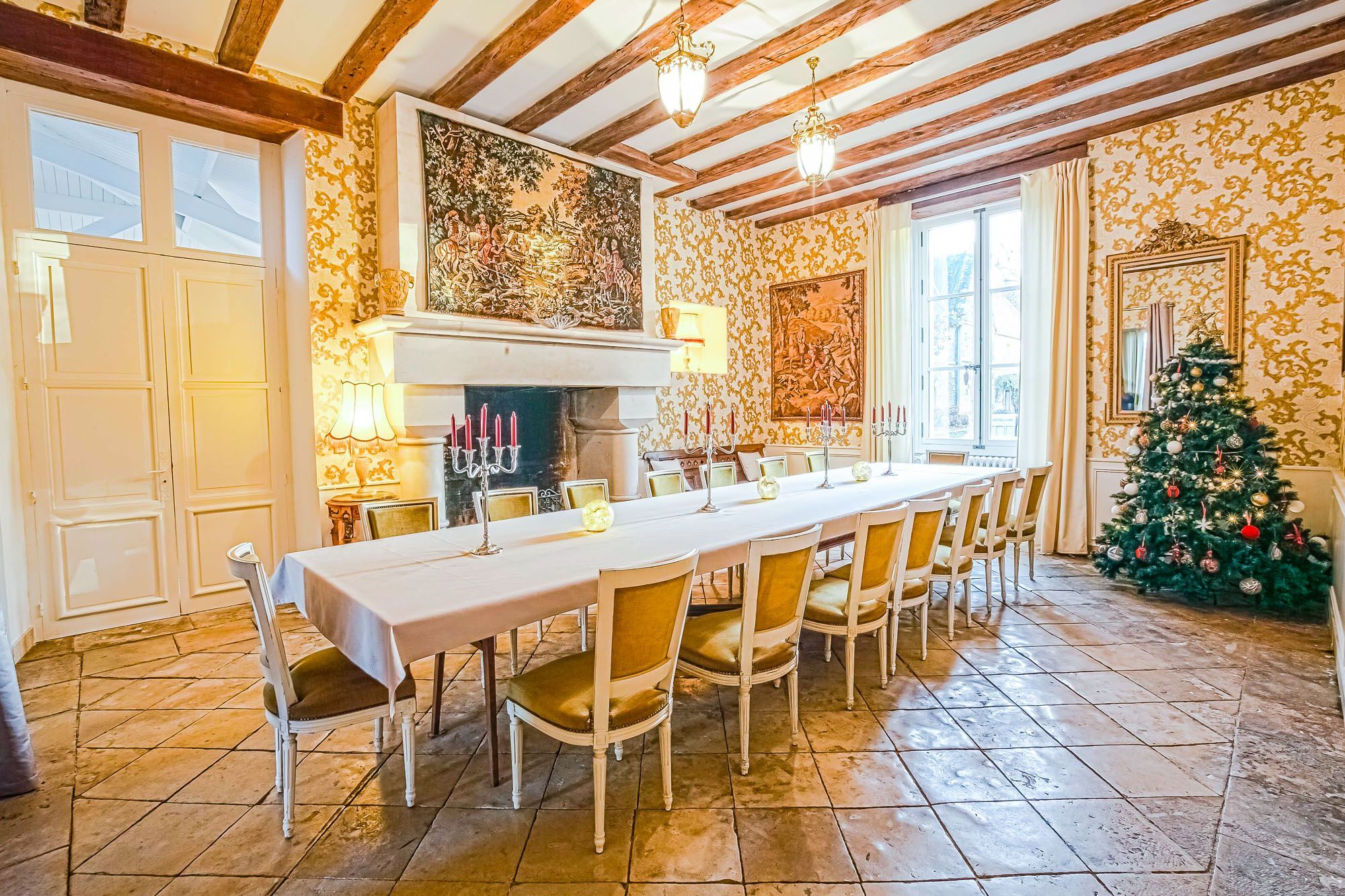 Un espace repas avec une longue table, des chaises, une cheminée et un sapin de Noël décoré.